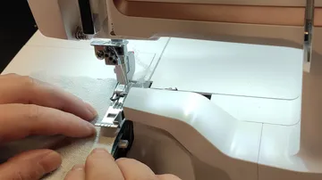 Hände führen den Stoff durch die Nähmaschine.