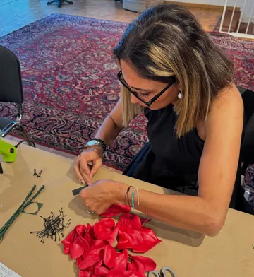 Person arranging red flower petals on table.
