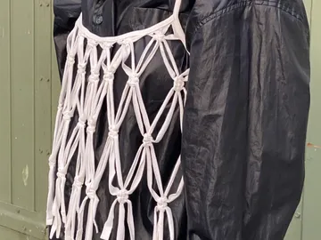 Someone wearing a black jacket against a green background is wearing a macrame top.