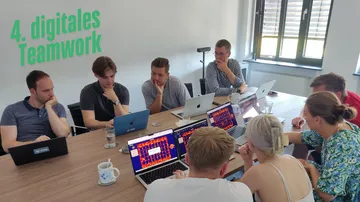 Gruppe von Leuten, die an einem Tisch mit Laptops arbeiten.