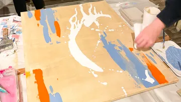 Hand paints abstract art on wooden board.
