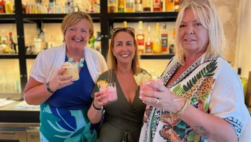 Drei Frauen halten Cocktails an einer Bar.