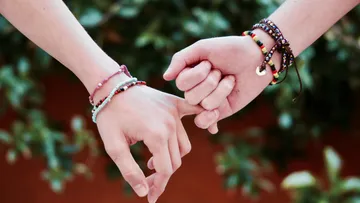 Two hands with bracelets, pinky fingers linked.