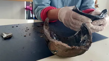 Person, die Keramikscherben auf dem Tisch hält und untersucht.