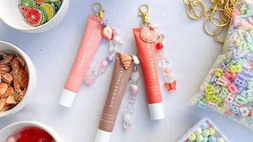 Drei Lipgloss-Tuben mit dekorativen Schlüsselanhängern.