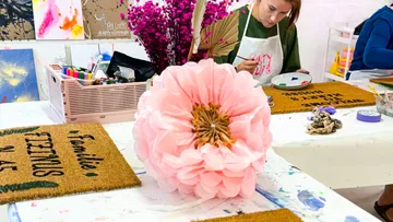 Person painting near large pink flower.
