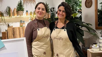 Two women smiling, wearing aprons in a plant store.
