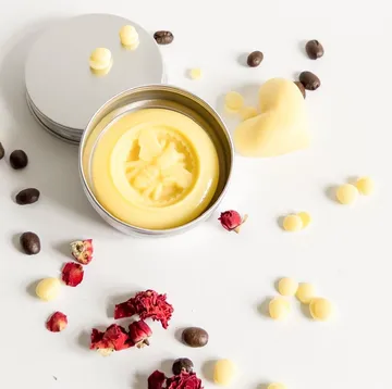 Tin of lotion bar with decorations on white surface.