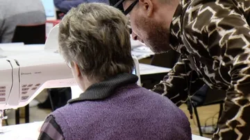 Person instructing another on sewing machine.
