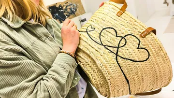 Woman paints hearts on woven basket indoors.