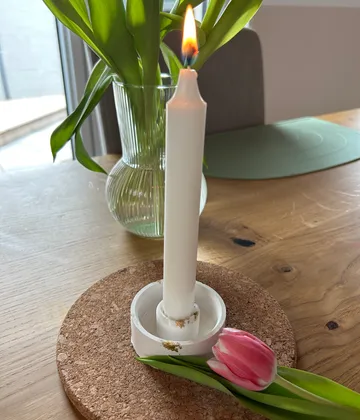 Brennende Kerze mit rosa Tulpe auf Korkmatte.