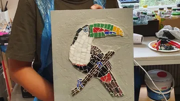 Person holding toucan mosaic artwork in workshop.