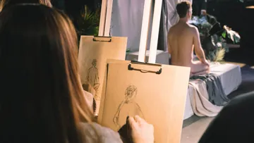 Artists sketching a nude model in studio.