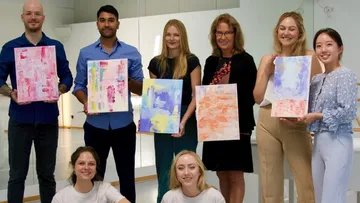 Group holding abstract paintings in studio.