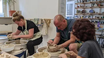 Three people shaping clay on pottery wheels in studio.