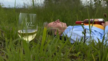 Person, die mit einer Weinflasche im Gras liegt.