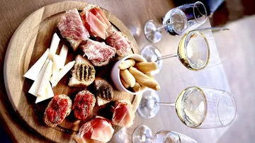 Wooden platter with charcuterie and wine glasses.