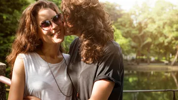 Couple embracing at lake in sunlight.