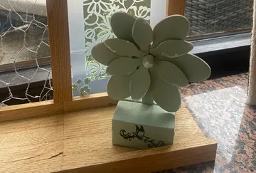 Green flower sculpture on wooden base by window.