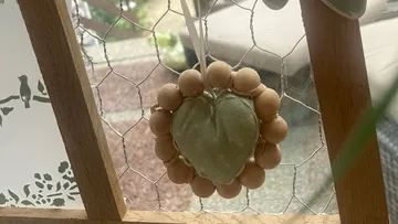 Herzdekoration mit Holzperlen an einem Fenster.