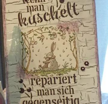 Illustriertes Schild mit Hasen, die sich unter einem Baum umarmen.