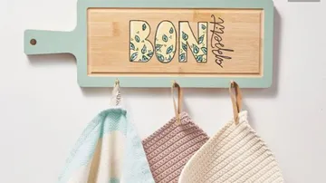 Decorative cutting board with colorful letters, towels hanging.