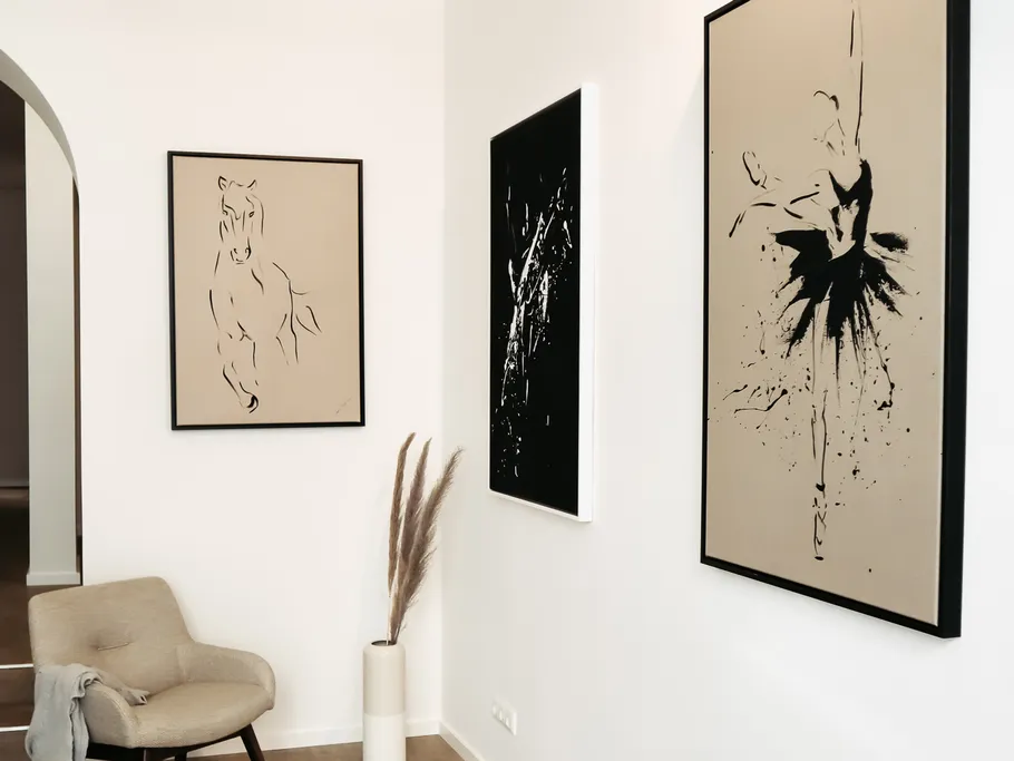 Three black and white paintings hang on a white wall.