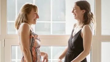Zwei lachende Frauen drinnen in der Nähe eines Fensters.
