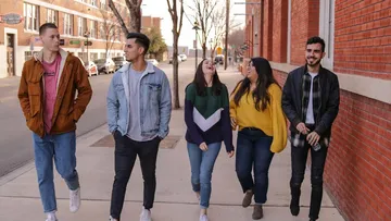 Five friends walking and laughing on the sidewalk.