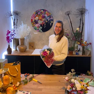 Smiling woman holds bouquet in flower shop.