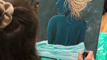 Person, die eine blaue Silhouette auf Leinwand malt.