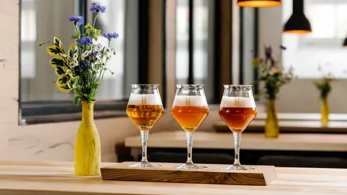 Three beer glasses on wooden tray, floral vase nearby.