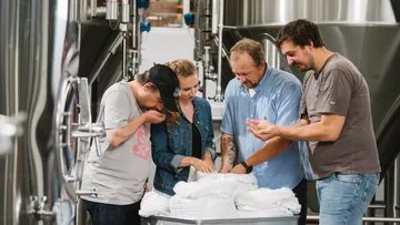 Vier Personen untersuchen Getreide in einer Brauerei.