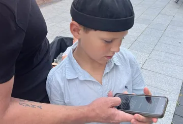 Kind schaut auf ein Smartphone, das von einem Erwachsenen gehalten wird.