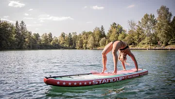 Person doing yoga on paddleboard in lake.