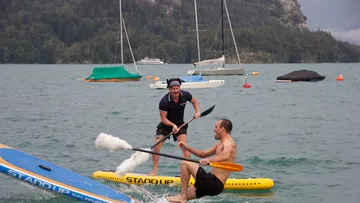 Zwei Männer paddeln spielerisch auf einem See.