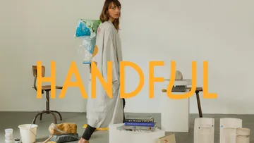 Woman in studio with art supplies, 'HANDFUL' overlay.