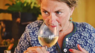Woman smells white wine in a glass indoors.