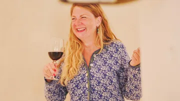 Frau hält ein Weinglas in der Hand und lacht drinnen.