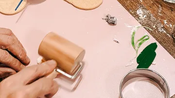 Hand rolling dough on pink surface.