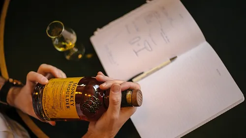 Person, die eine Whiskyflasche neben dem Notizbuch hält.