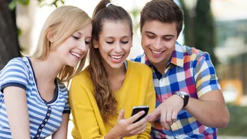 Three friends looking at a smartphone outdoors.