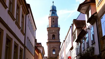 Tall church tower between narrow street buildings.