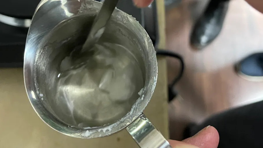 Stirring milk froth in metallic pitcher.