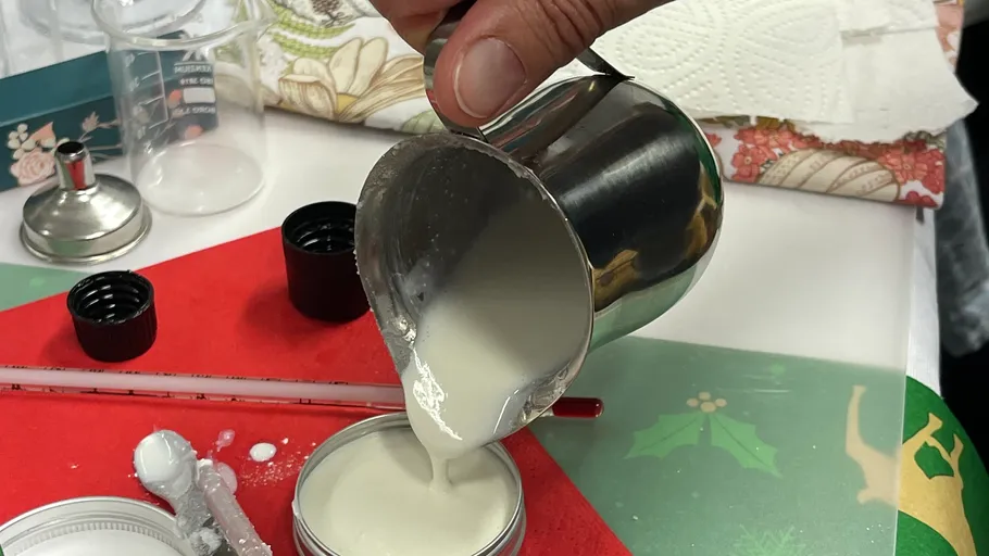 Hand pouring liquid into container on table.