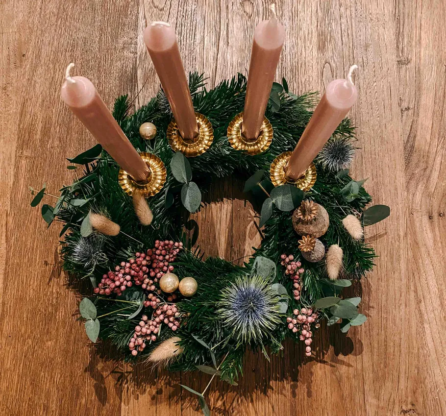 Adventskranz mit rosa Kerzen auf Holzoberfläche.