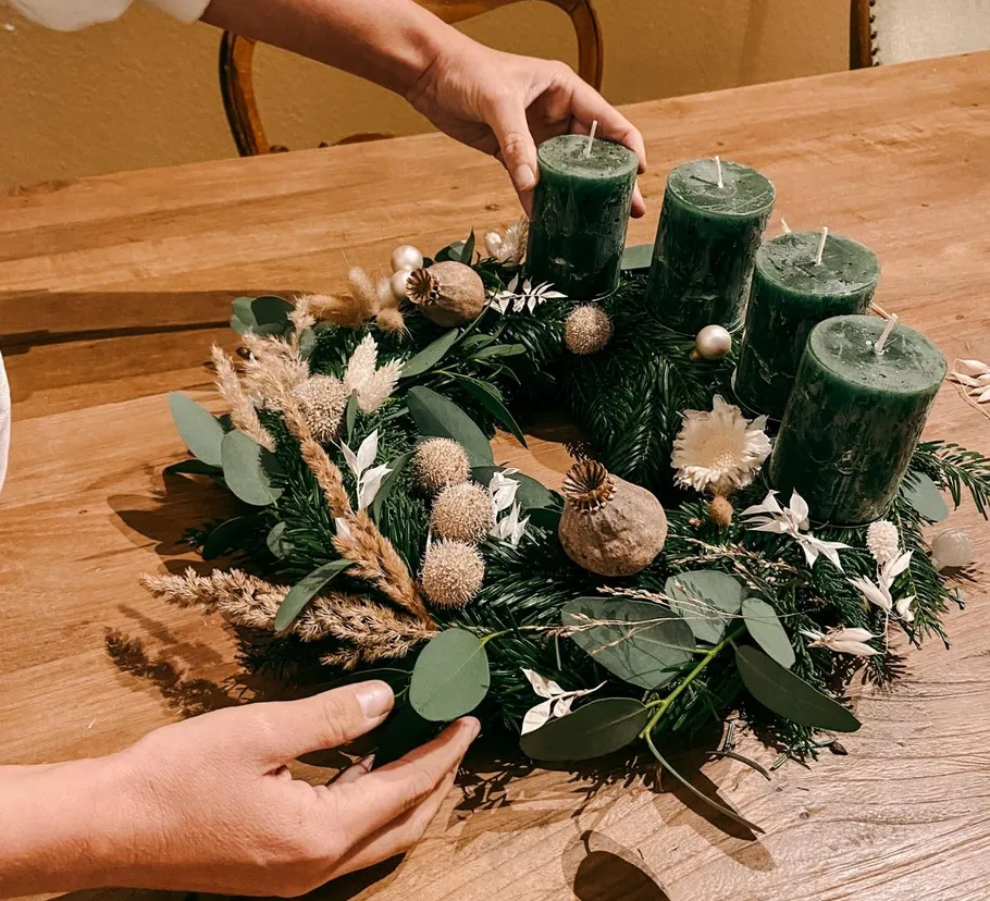 Hands adjusting wreath with green candles on table.