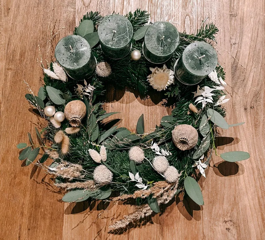 Festive wreath with green candles on wood surface.