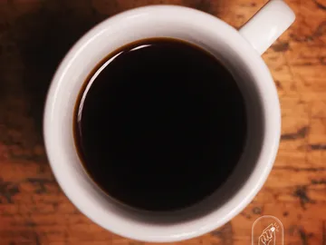 A black cup of coffee is sitting on a wooden table.