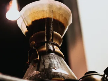 Glaskanne brüht Kaffee unter warmem Licht in Küche.